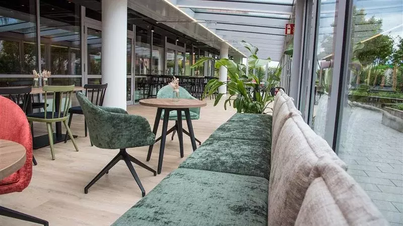 Interiér moderní jídelny s místy k sezení u okna, stoly, židlemi a rostlinami.