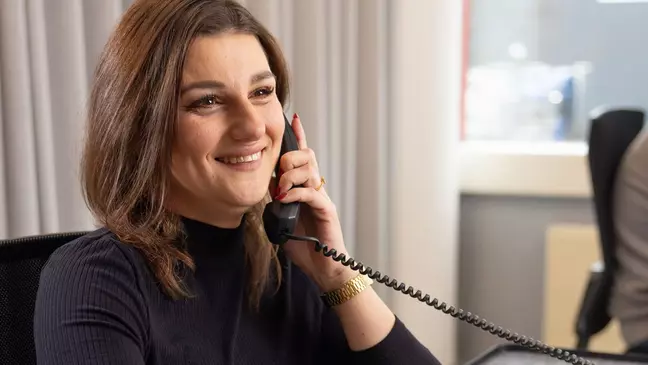 Eine Frau telefoniert während sie am Arbeitsplatz sitzt und lächelt