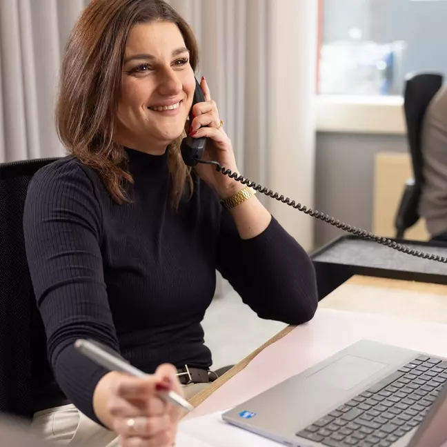 žena telefonuje, zatímco sedí na svém pracovišti a usmívá se