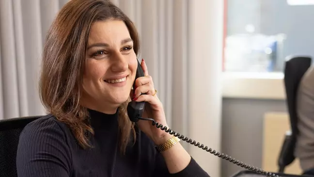 Žena telefonuje, zatímco sedí na svém pracovišti a usmívá se