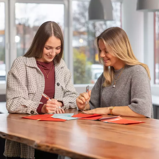 Zwei Mitarbeitende schreiben gemeinsam an einem Tisch in einem modernen Besprechungsraum.