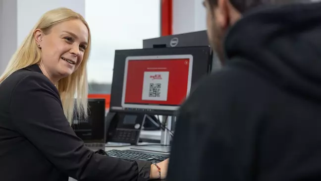 Eine Frau und ein Mann sitzen vor einem Computer, die Frau lächelt und wendet sich dem Mann zu