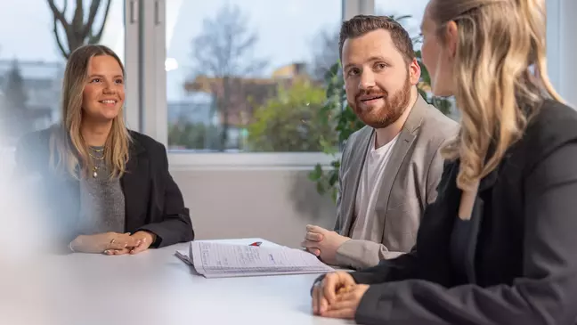 Zwei Frauen und ein Mann sitzen an einem Tisch und sprechen miteinander